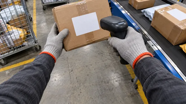 Cámara 4: una mano sostiene un paquete mientras la otra lo escanea con un lector de códigos.