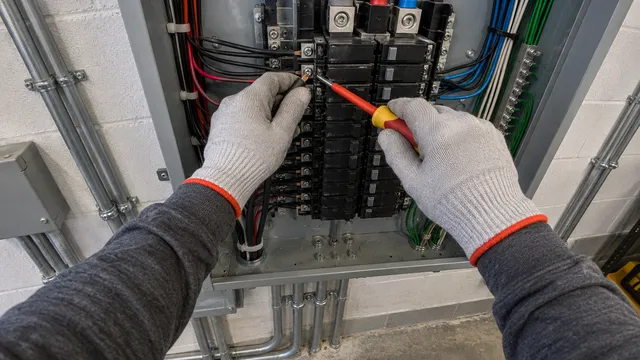 Cámara 9: una mano sostiene un cable mientras la otra aprieta un tornillo de un tablero eléctrico.